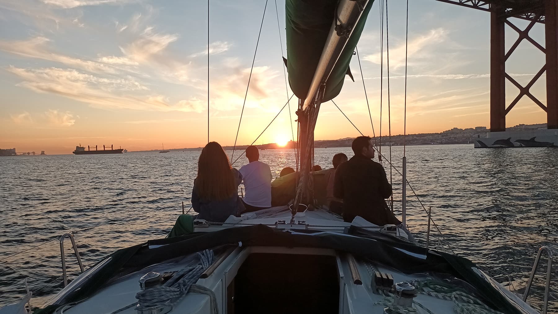 Group sailing toward sunset under bridge on calm harbor waters