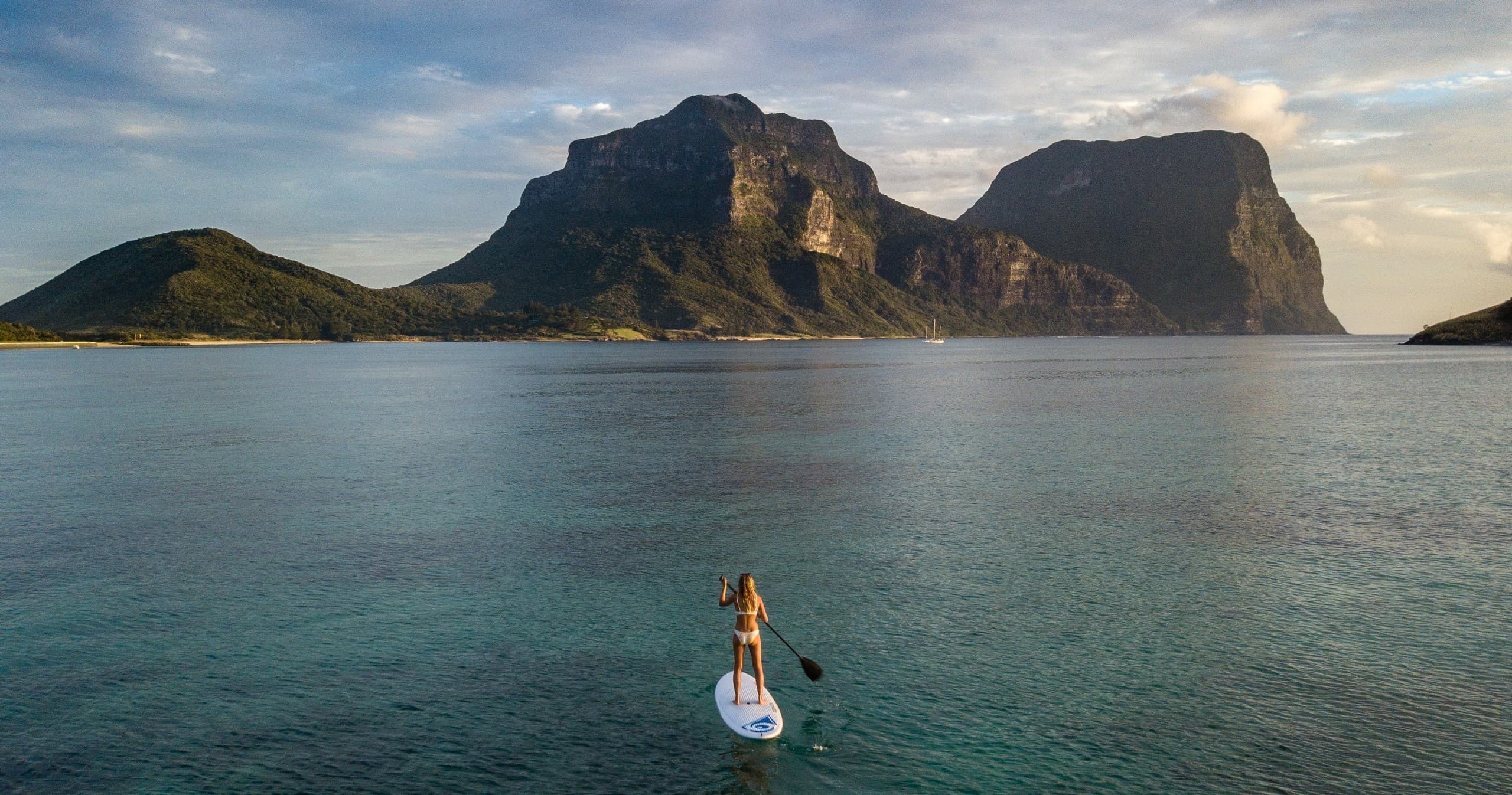 Stand-up paddleboarder heading toward dramatic island peaks