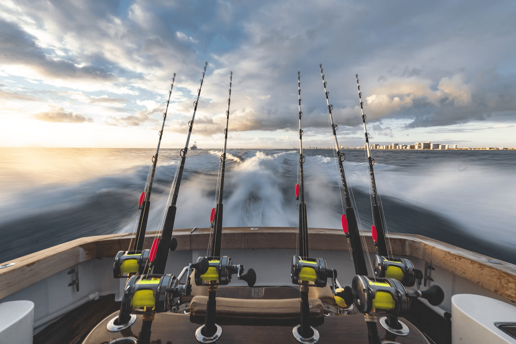 Sportfishing rods on boat heading through ocean at sunrise