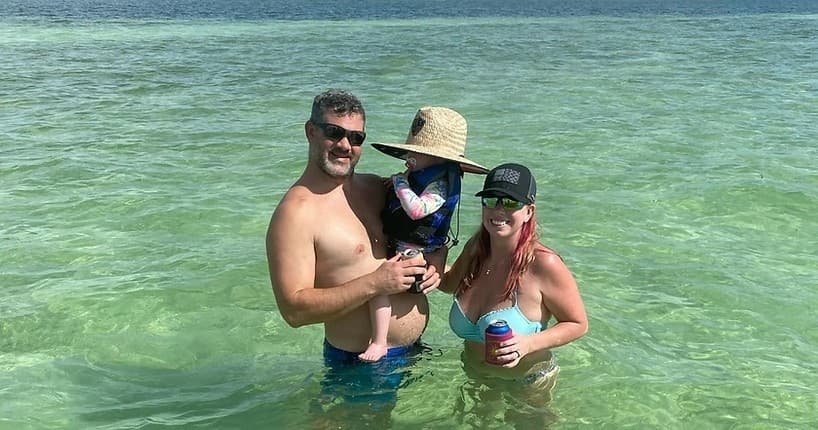 Family wading in clear shallow Gulf waters holding child near shore