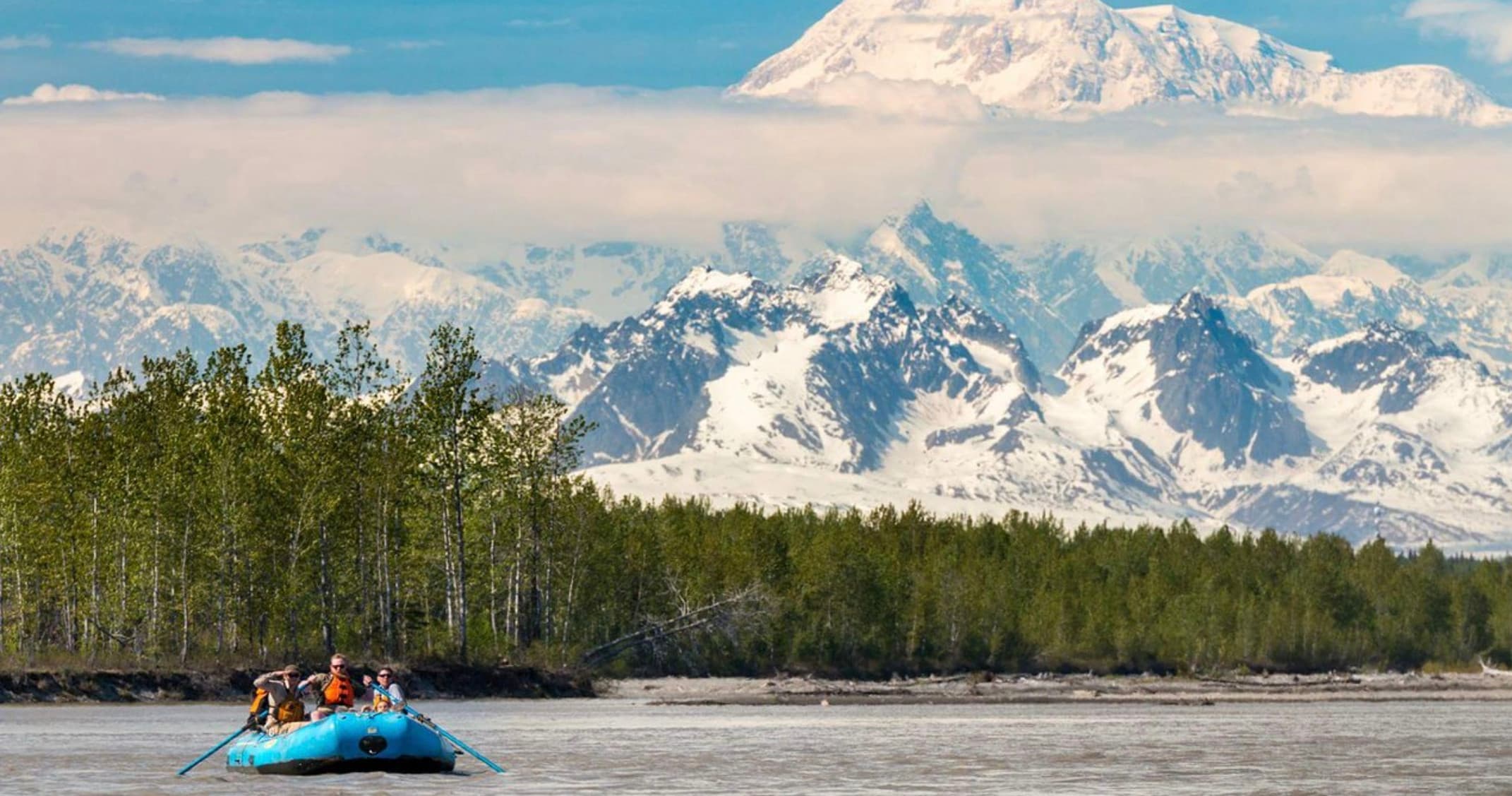 Rafting on Alaskan river with snowcapped mountains backdrop
