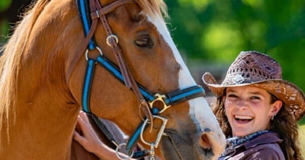 Young girl with chestnut horse smiling at summer riding camp