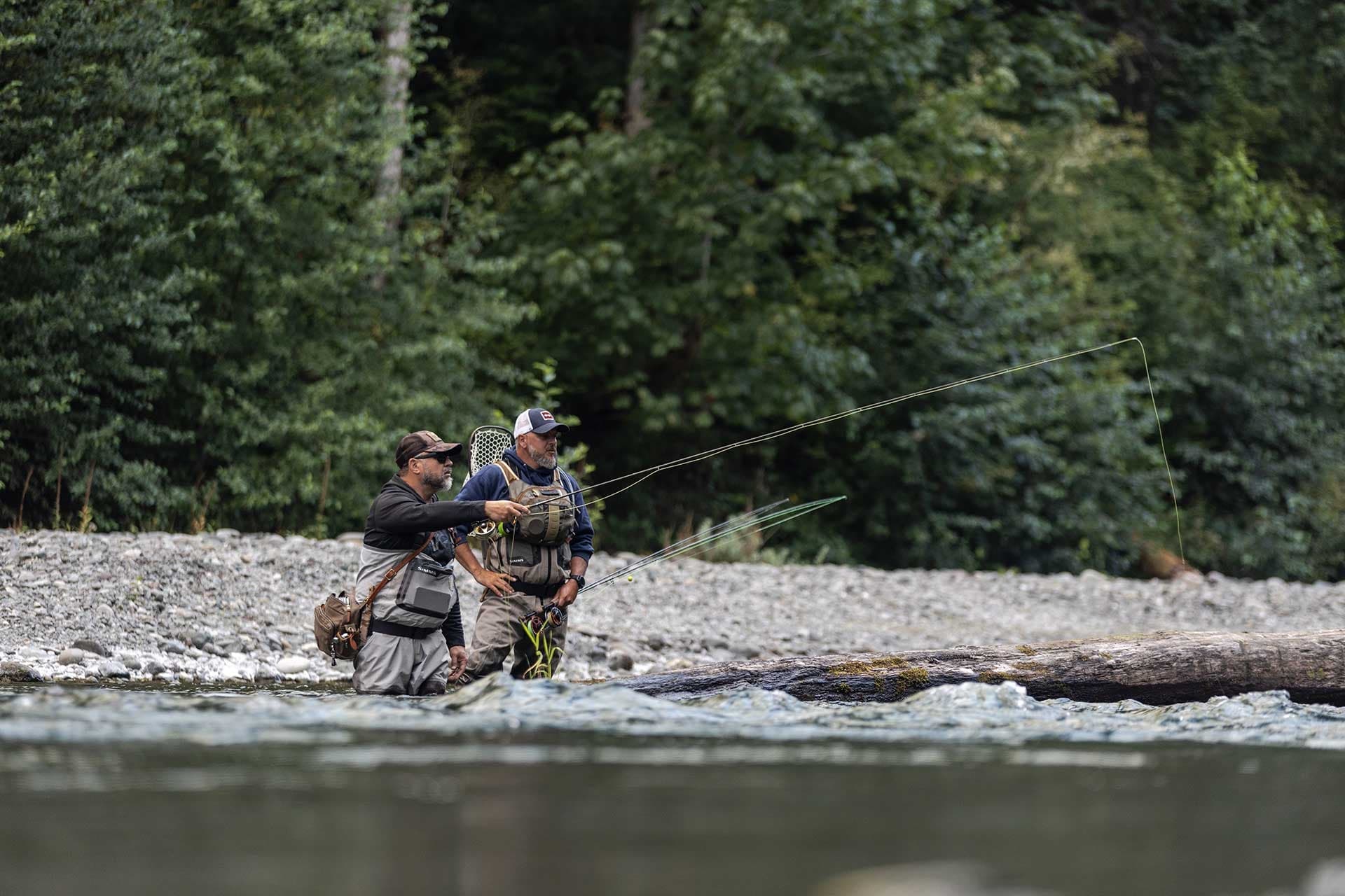 Two fly anglers wading a gravel river teaching technique