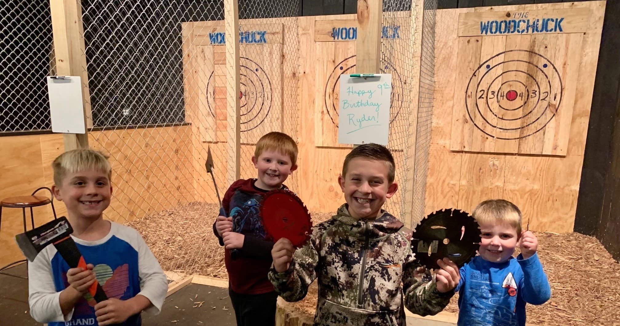 Kids holding axes and target discs in indoor axe-throwing lane