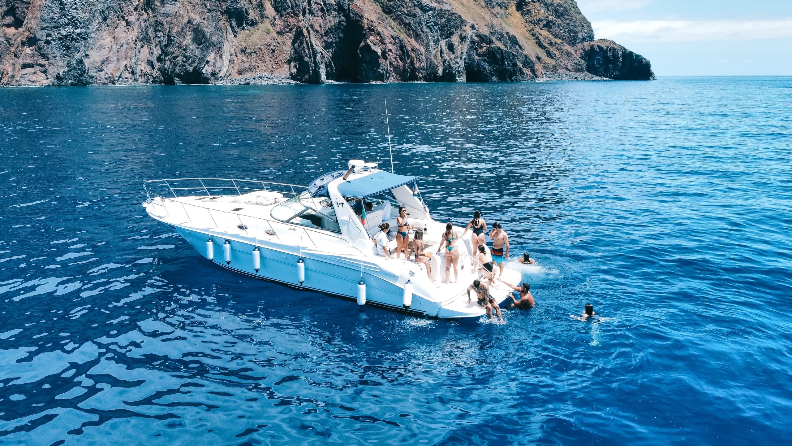 Coastal boat excursion near rocky cliffs with swimmers diving