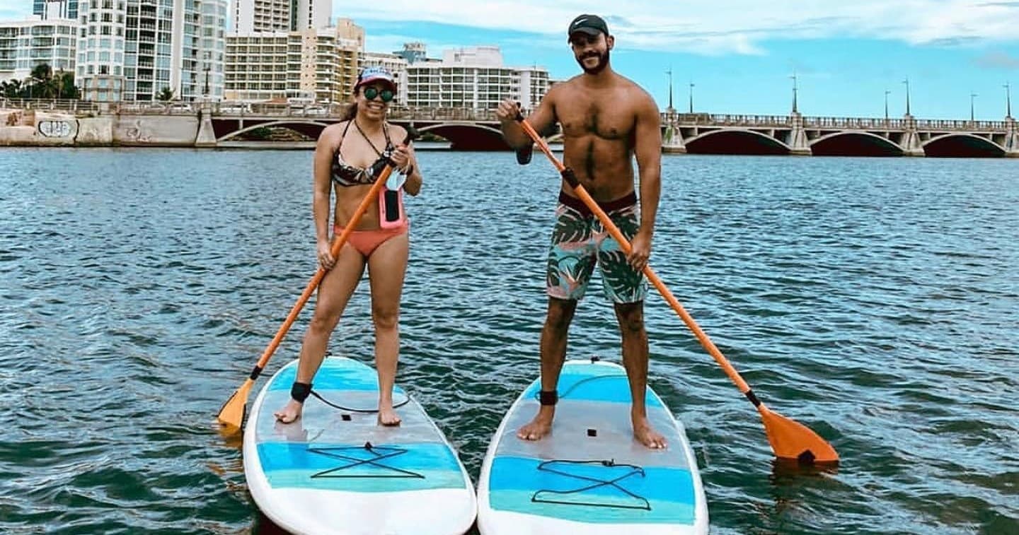 Couple stand-up paddleboarding in urban waterway with bridges