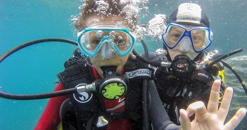 Close-up scuba divers underwater giving OK sign during ocean dive