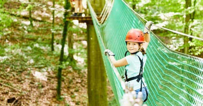 Child wearing helmet navigating suspended net bridge in forest adventure