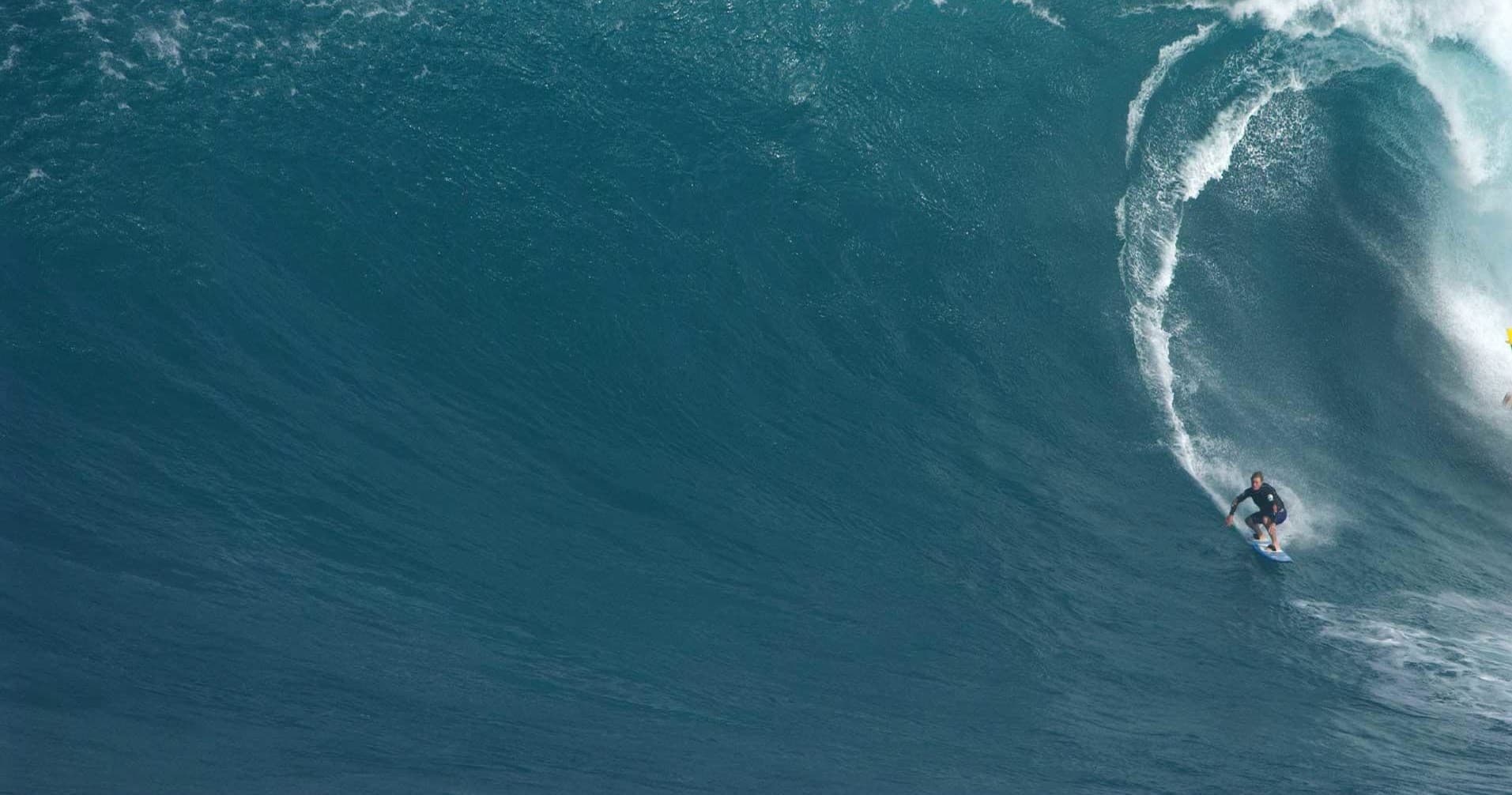 Surfer riding a massive blue ocean wave off a reef