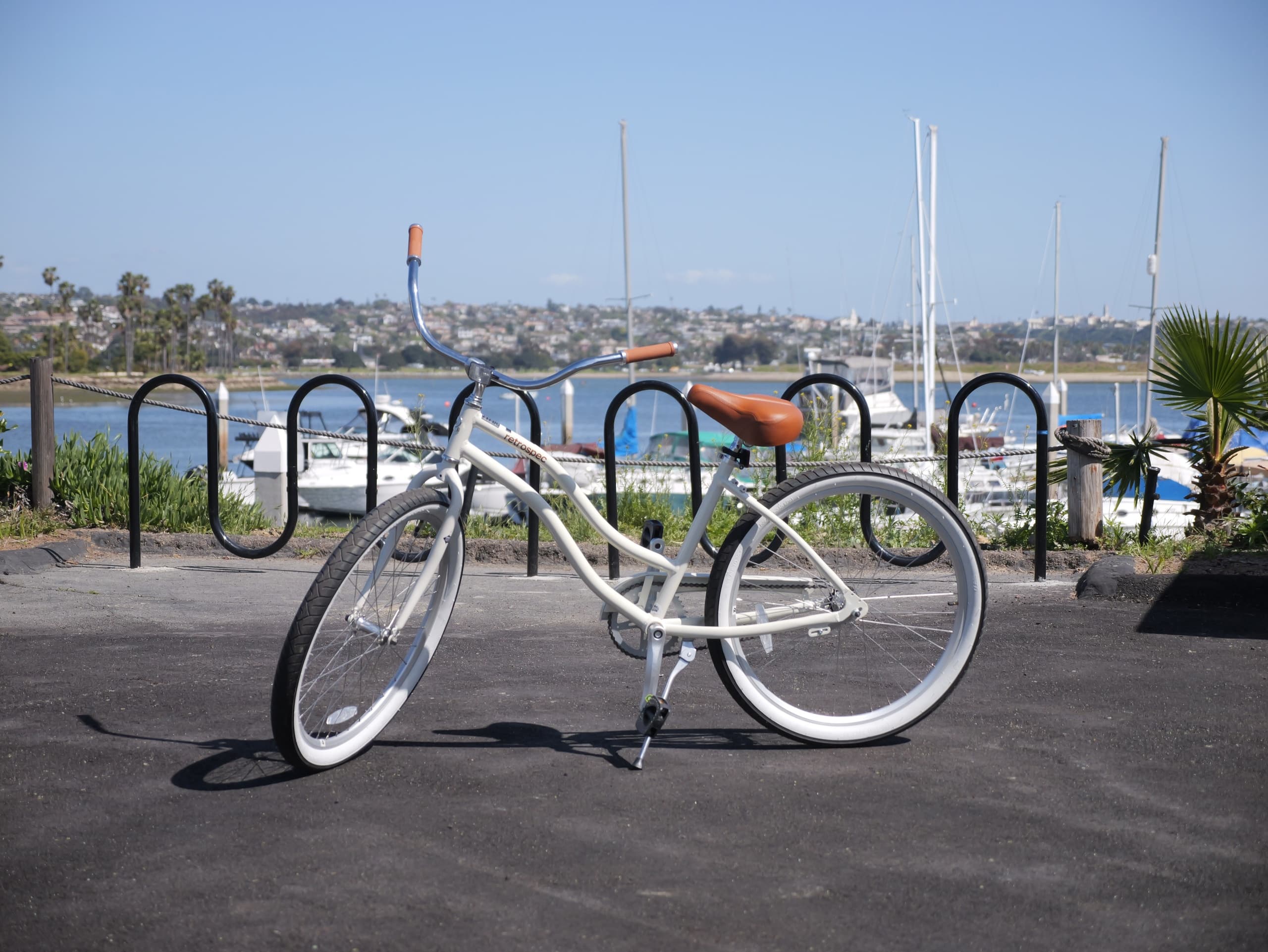 White cruiser bike parked on waterfront path with marina views
