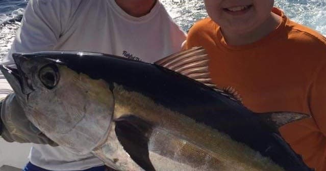 Anglers holding large yellowfin tuna on charter fishing boat deck