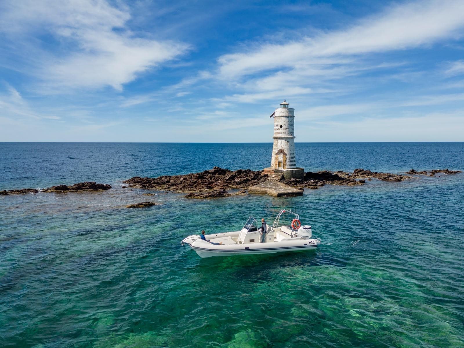 Small boat by rocky lighthouse, coastal sightseeing excursion