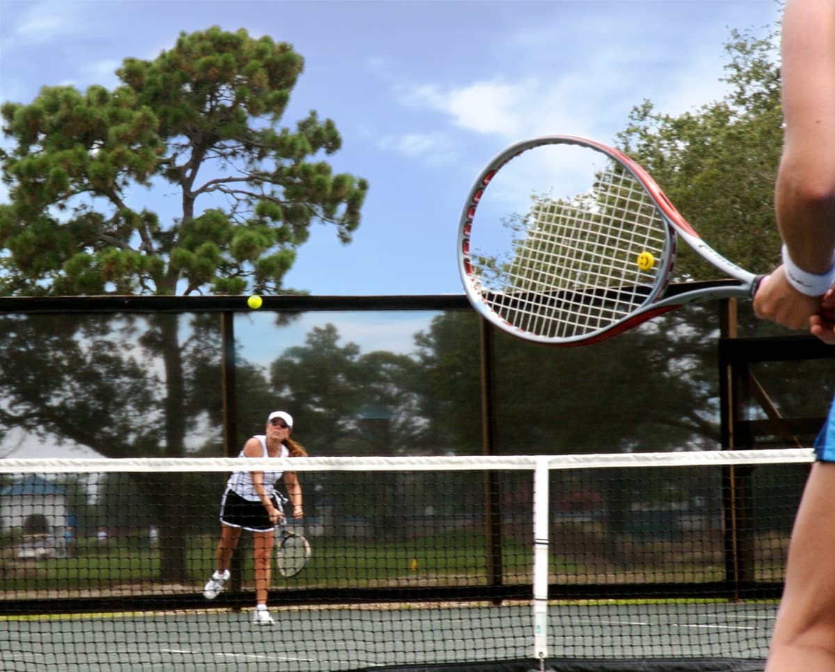Tennis players rallying on outdoor court under trees