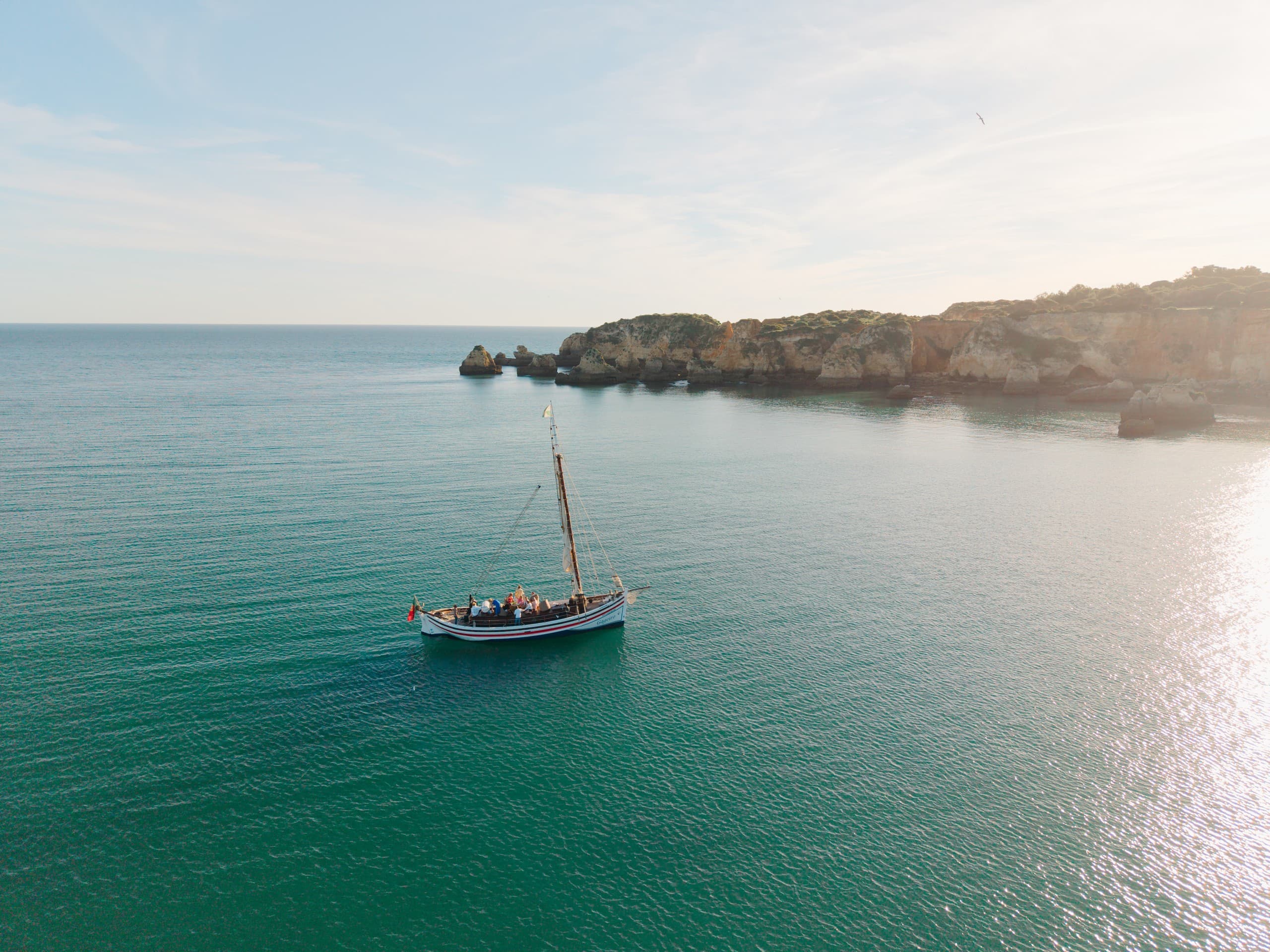 Sailboat sailing in clear green bay with coastal cliffs