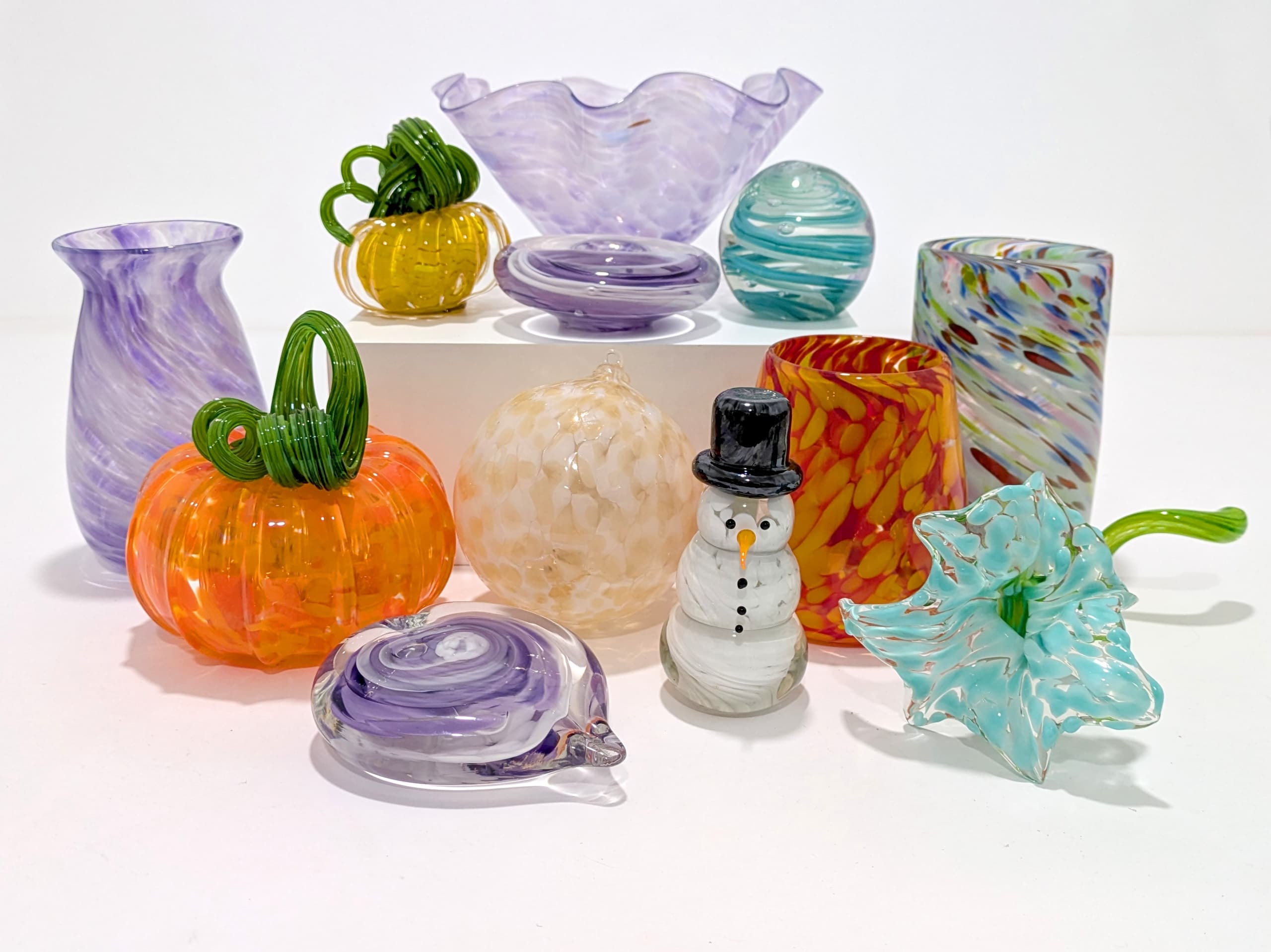 Assorted hand-blown glass ornaments and vases on white backdrop