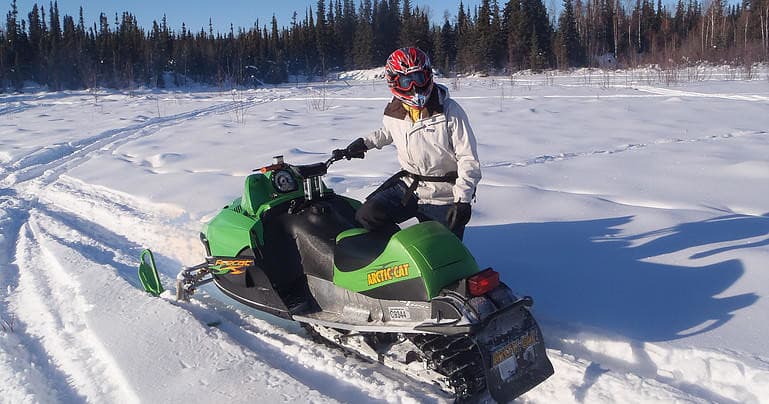 Snowmobile rider on green sled riding across packed snow trail