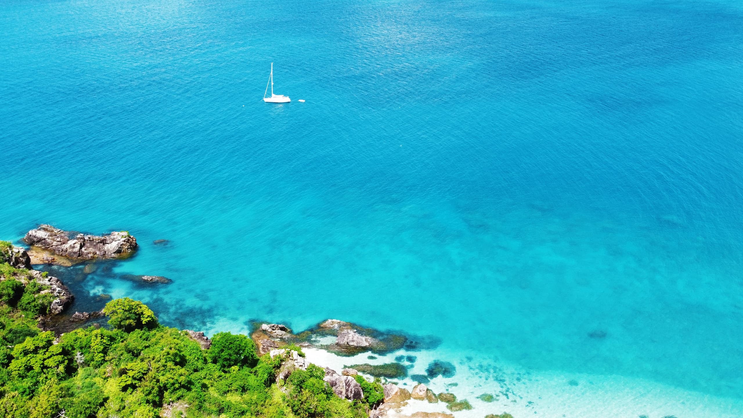 Aerial turquoise coast with lone sailboat near coral reef