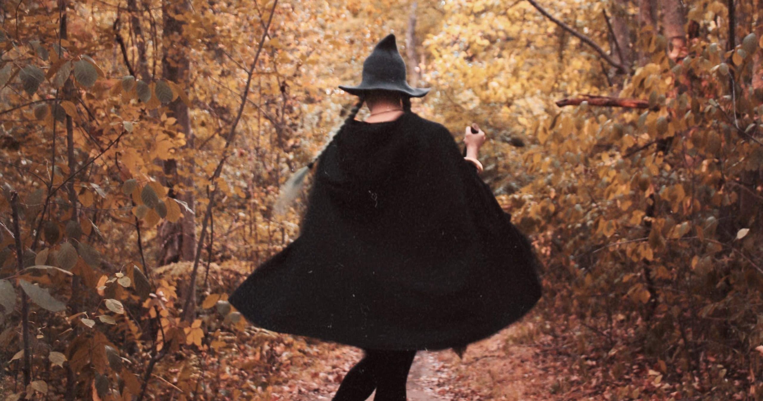 Witchlike figure walking through autumn forest trail