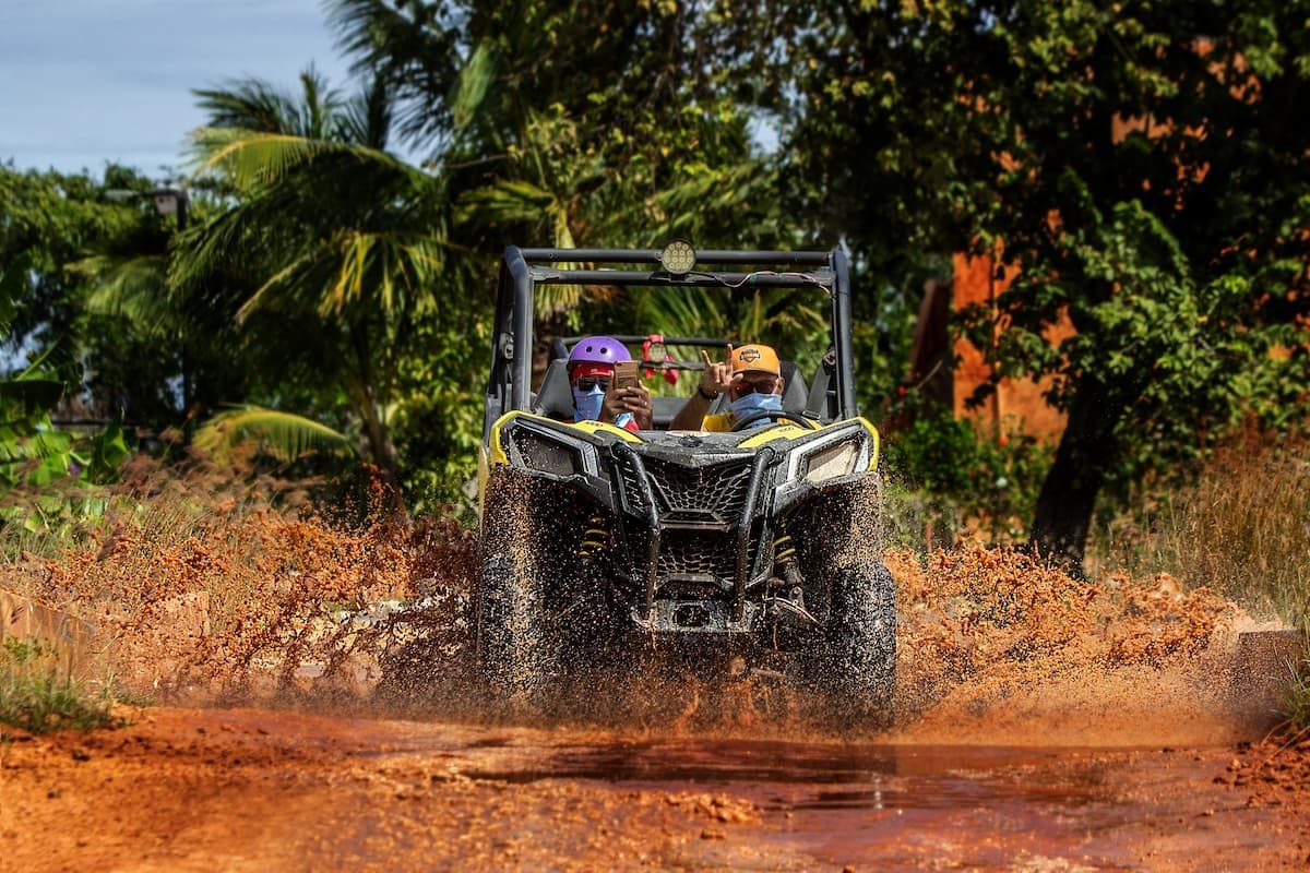 Off-road ATV riders splashing mud through tropical dirt trail adventure