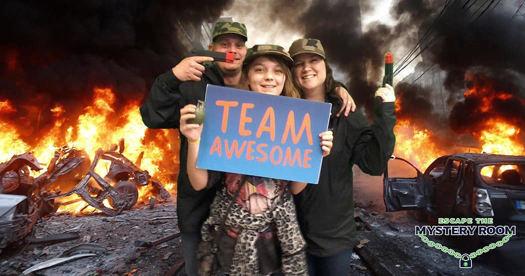 Team holding 'Team Awesome' sign with fiery wreckage backdrop
