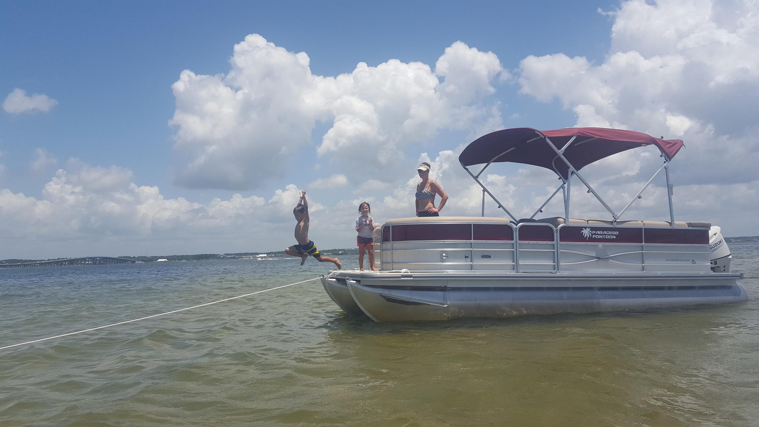 Family jumping from pontoon into shallow bay under clouds