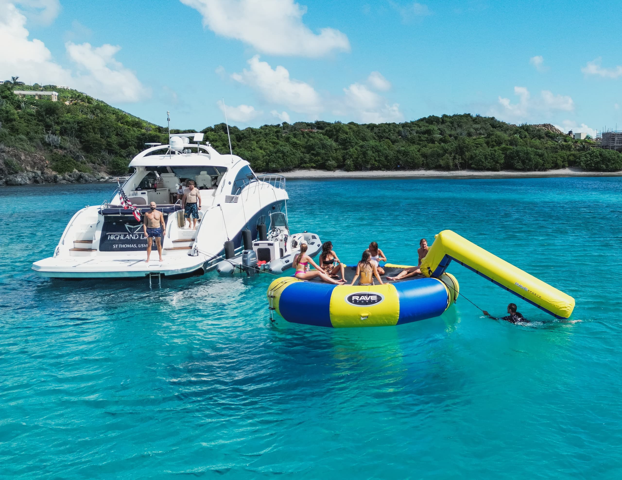 Families enjoying inflatable water trampoline beside charter yacht