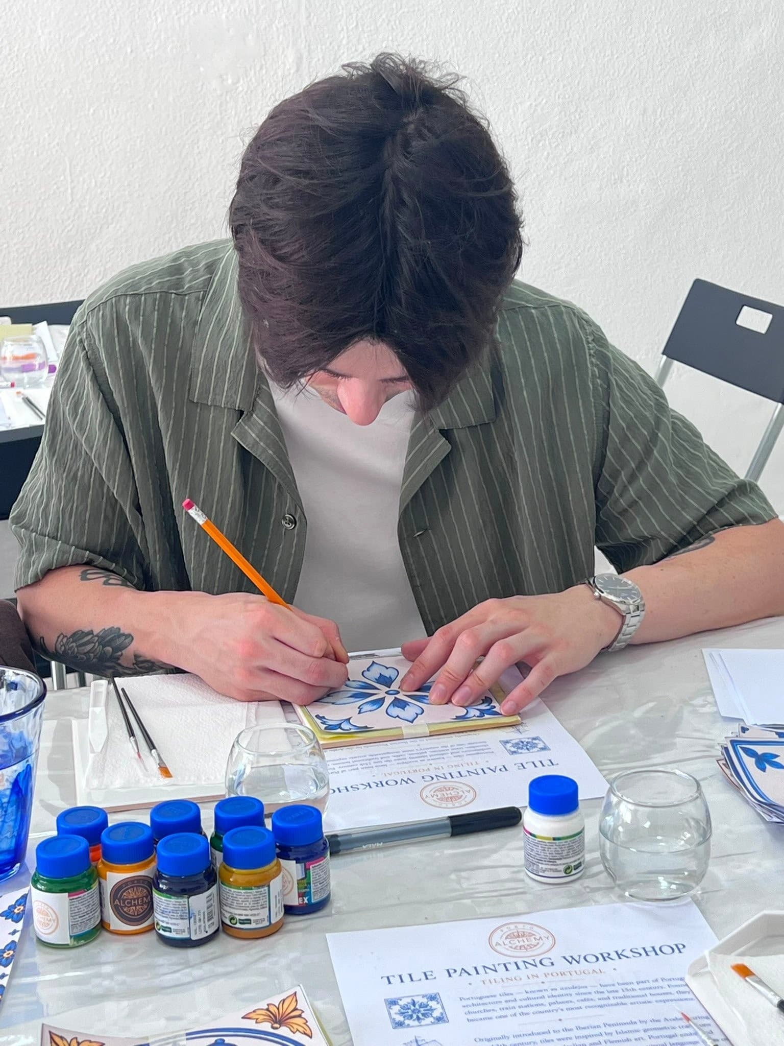 Artist painting ceramic tile at indoor workshop table, focused
