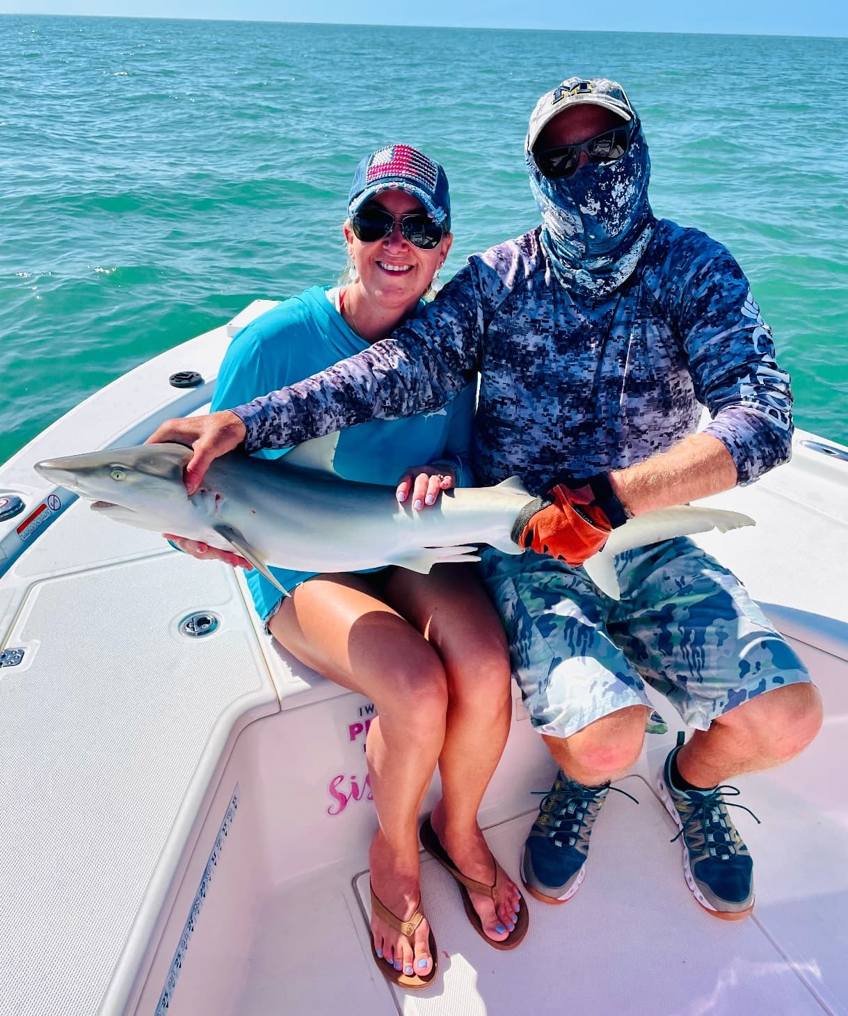 Couple aboard flats boat holding a small shark in turquoise water