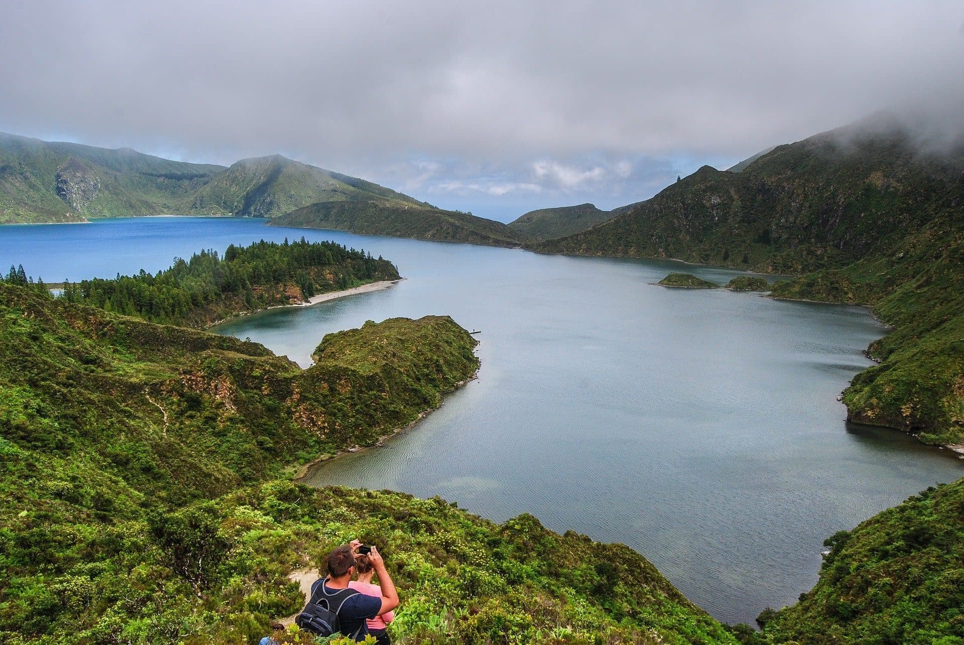 Hiker overlooking rugged lake inlet and green cliffs in Azores