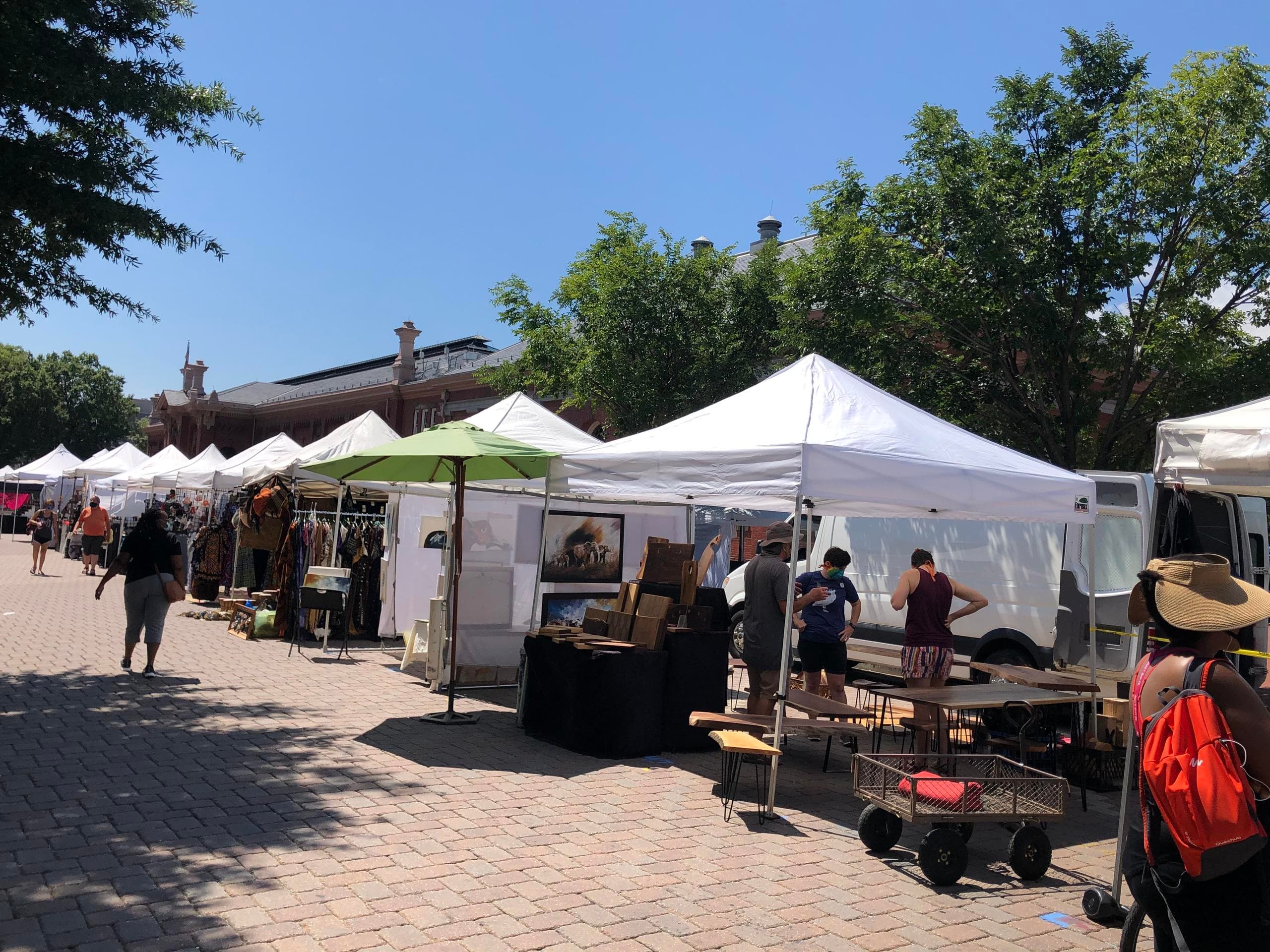 Outdoor artisan market stalls under trees on sunny plaza