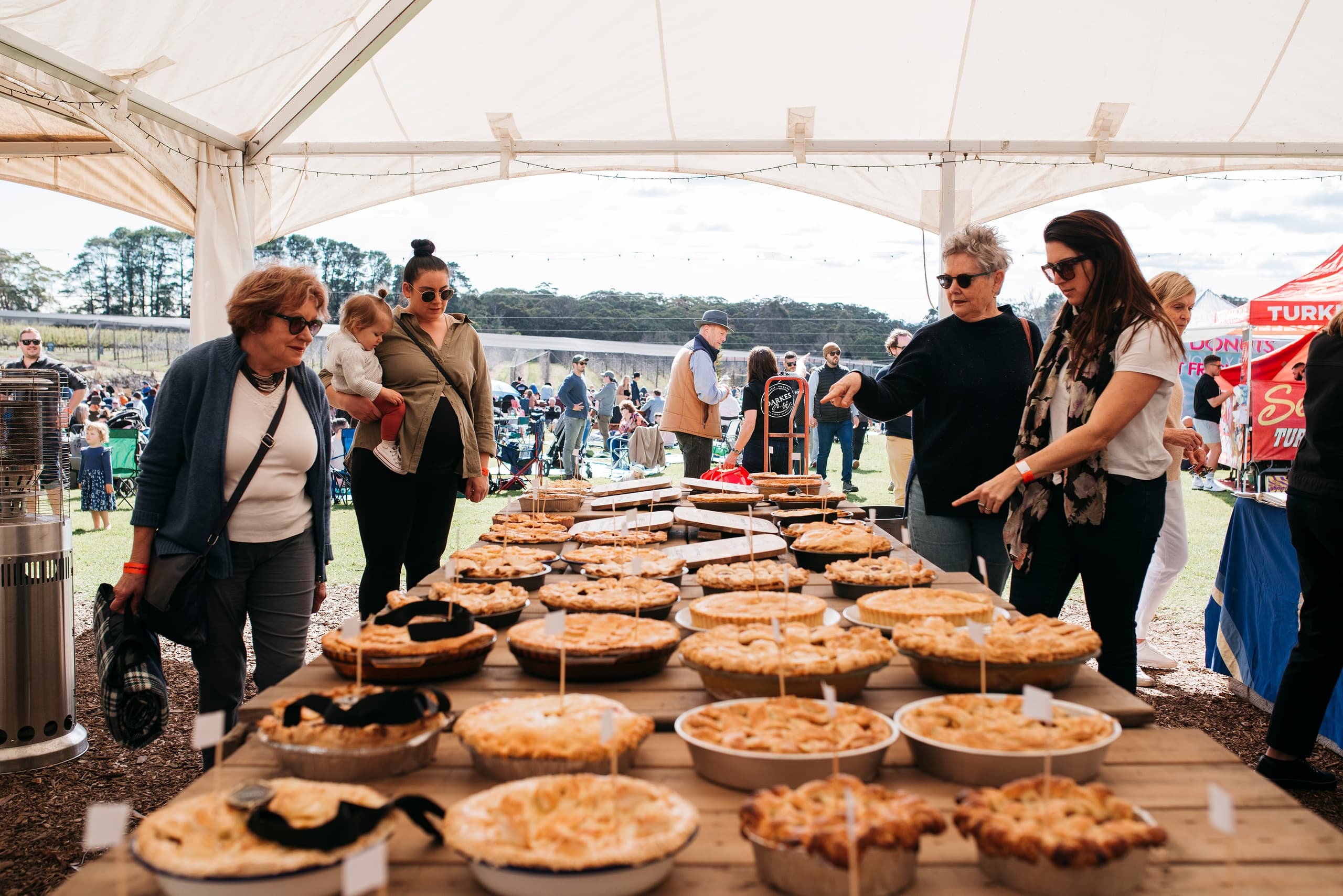Outdoor pie festival under tent with visitors sampling desserts