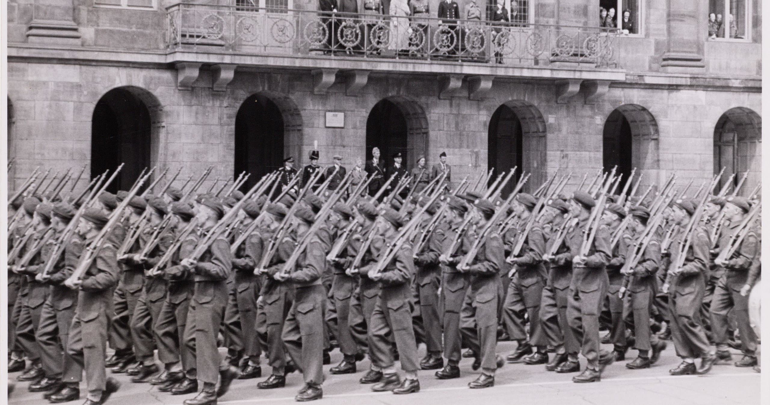 Soldiers marching in formation down urban street, historic military parade