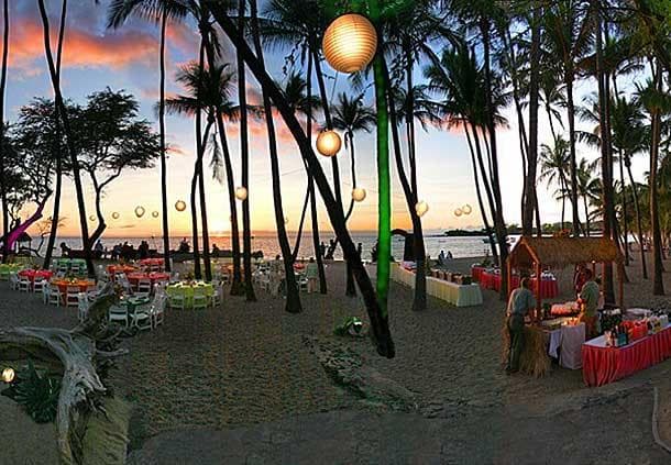 Beach luau setup with palm trees, lanterns at sunset