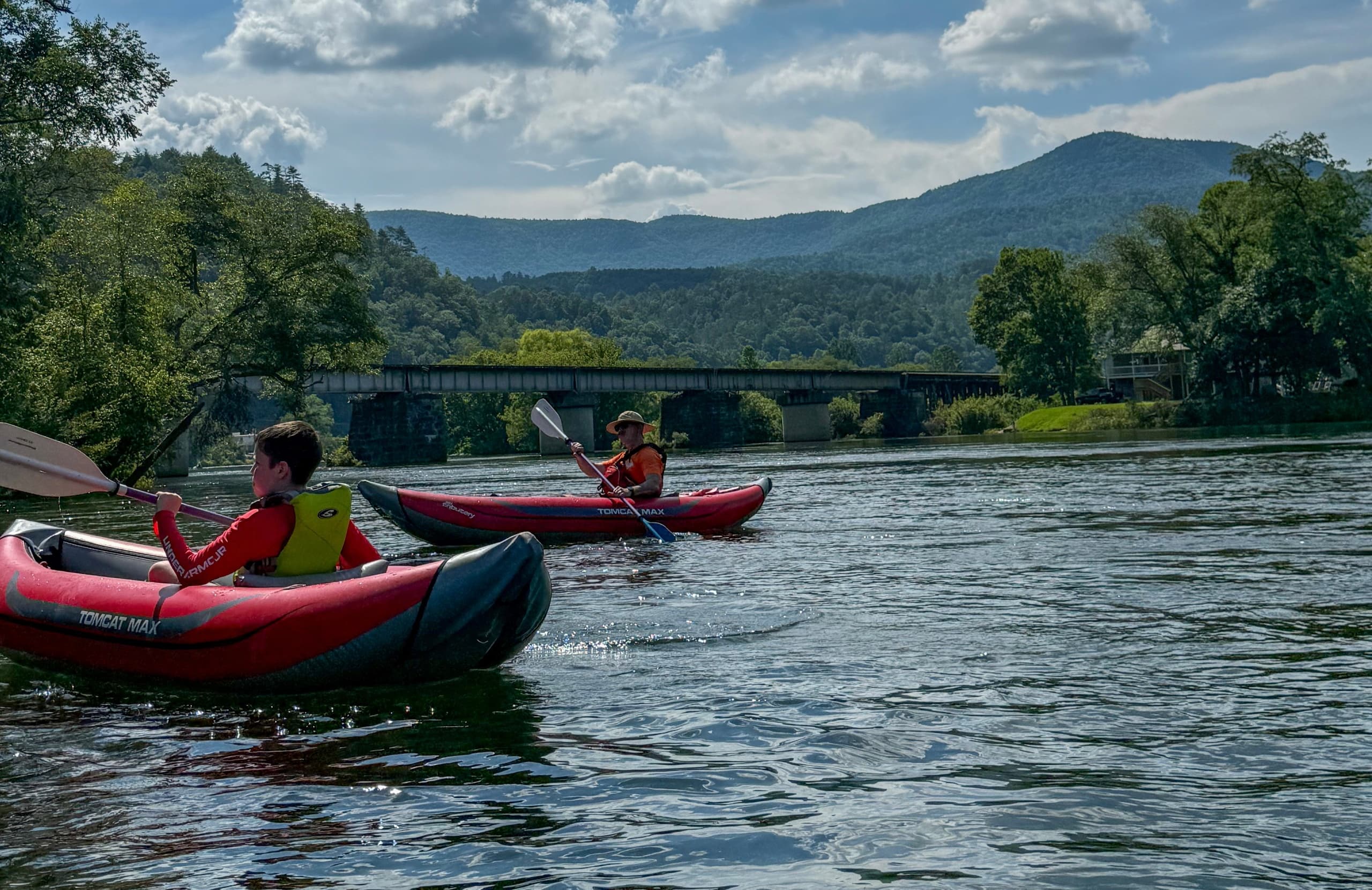Two kayakers paddling scenic river with distant mountain views