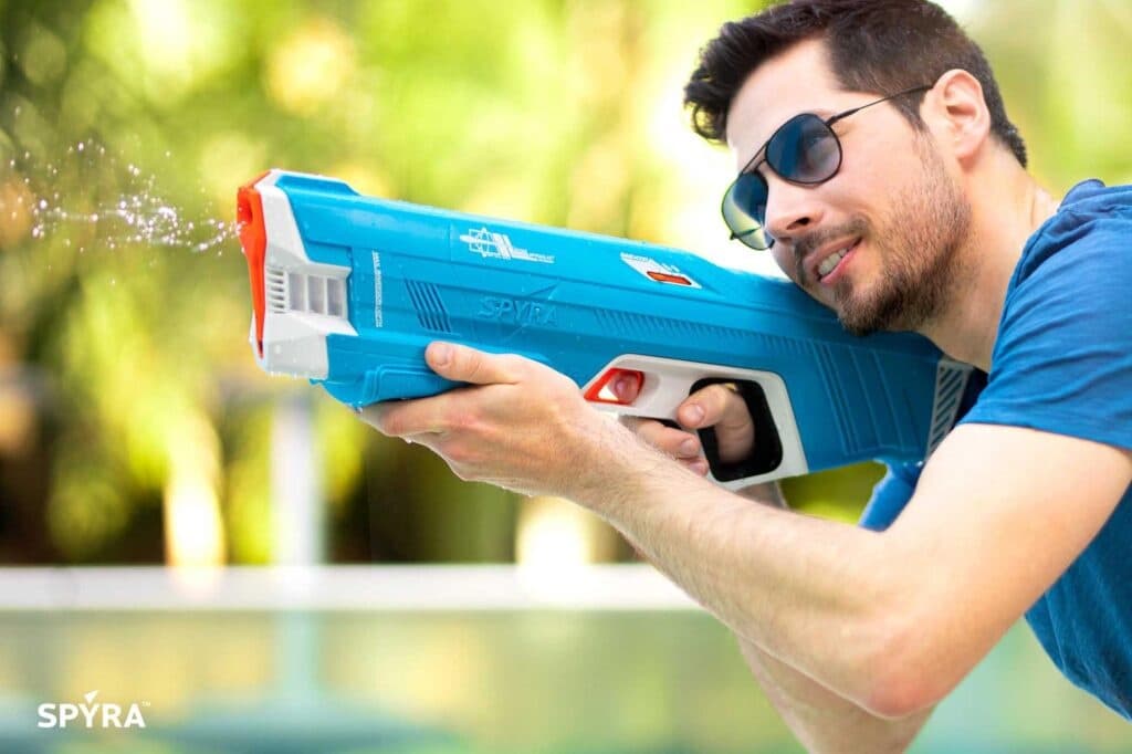 Man aiming a blue water blaster near pool in sunny park