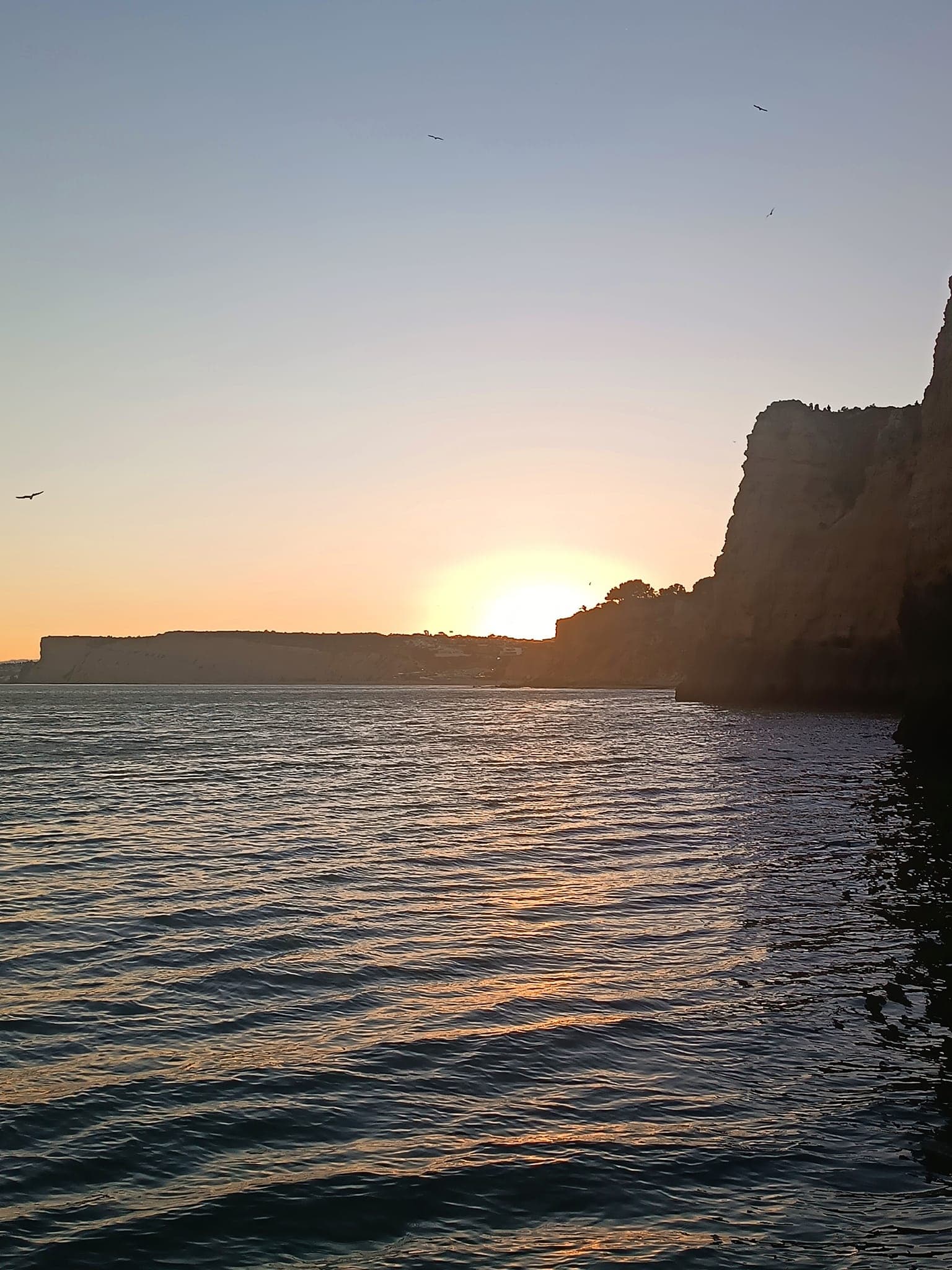 Sunset over sea and coastal cliffs with calm waters at dusk