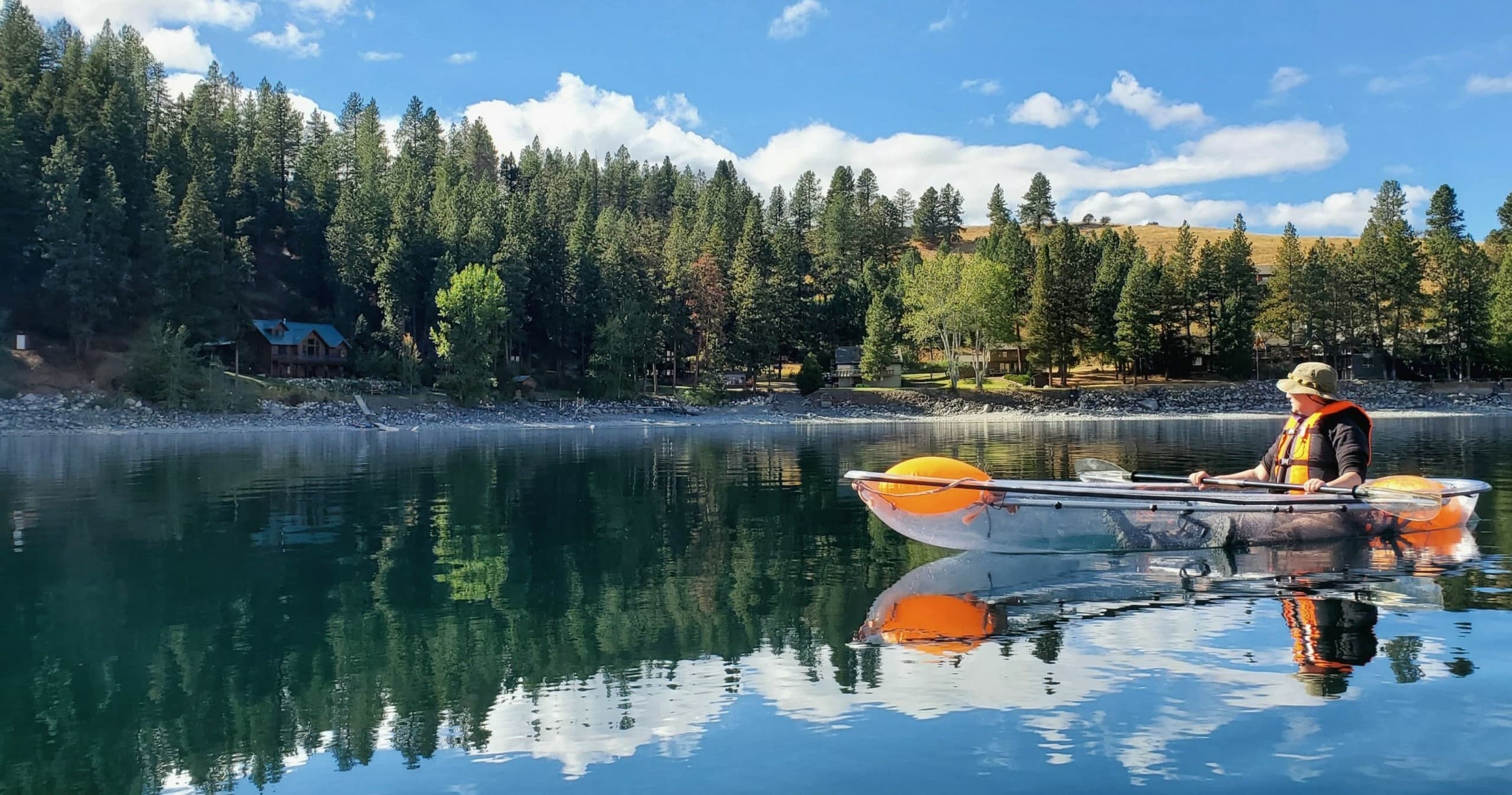 Kayakers paddling on reflective mountain lake with forest shore
