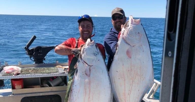 Two anglers holding halibut on open ocean during deepsea charter