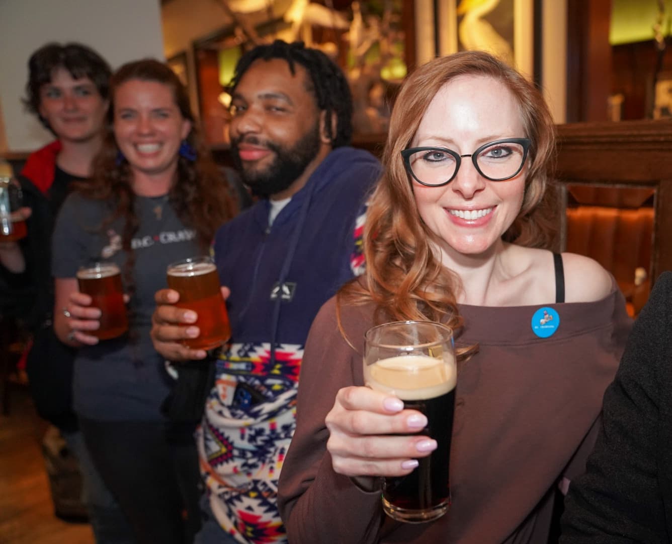 Group holding craft beers in crowded indoor pub during bar crawl