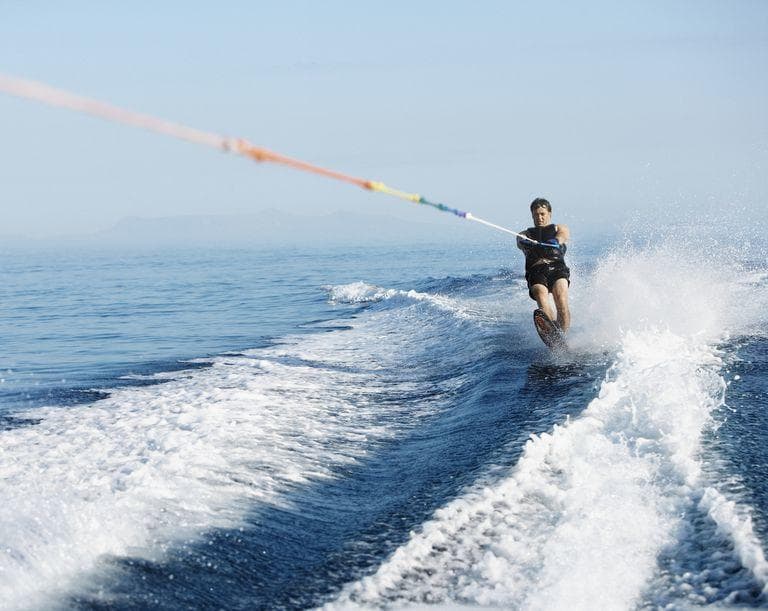 Waterskier carving wake on open ocean near coastal horizon