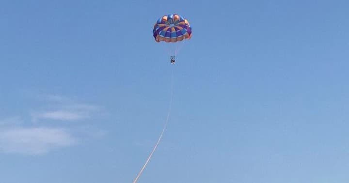Single parasailer trailing long towline against clear blue sky ocean