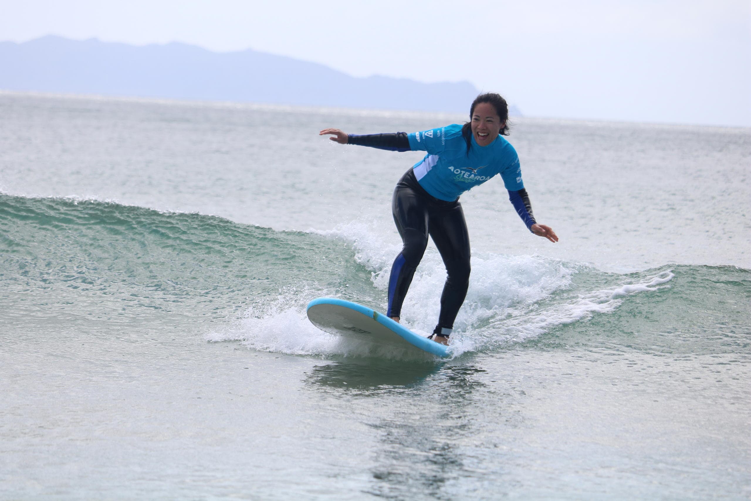 Solo surfer balancing on gentle wave near rocky shoreline