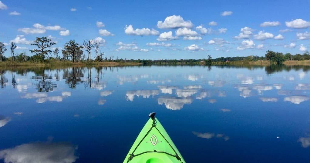 Green kayak prow on calm reflective marsh lake with blue sky
