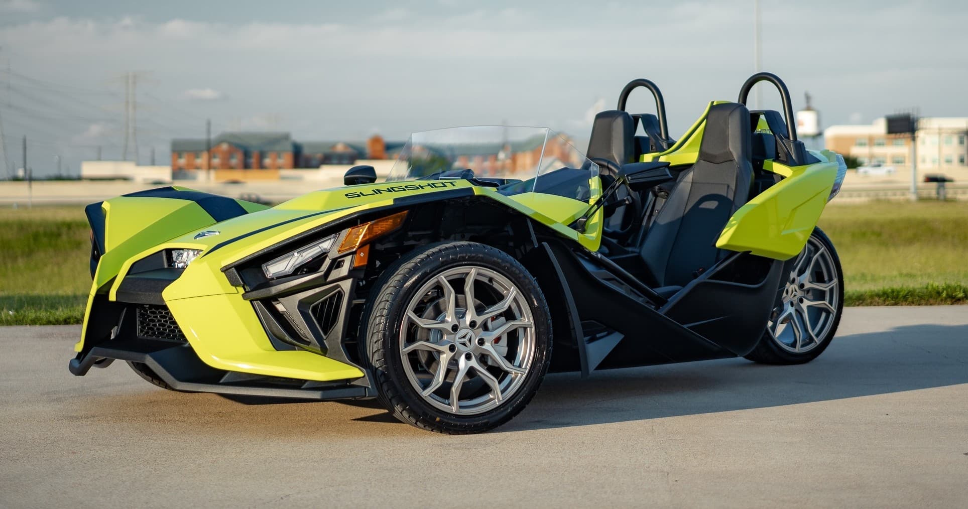 Vibrant lime Slingshot parked on roadside grass under blue sky
