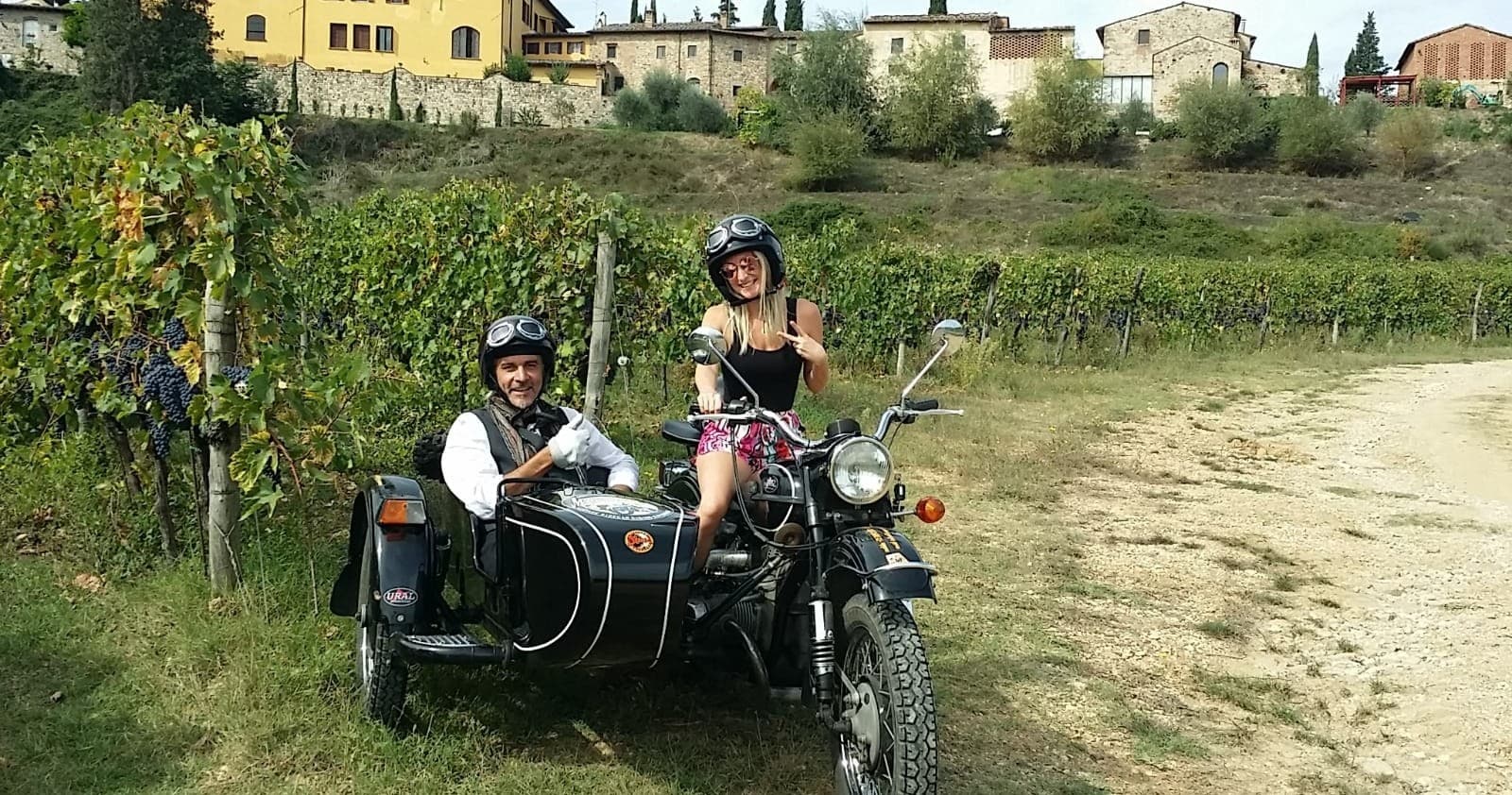 Couple riding vintage sidecar motorcycle through vineyard trails