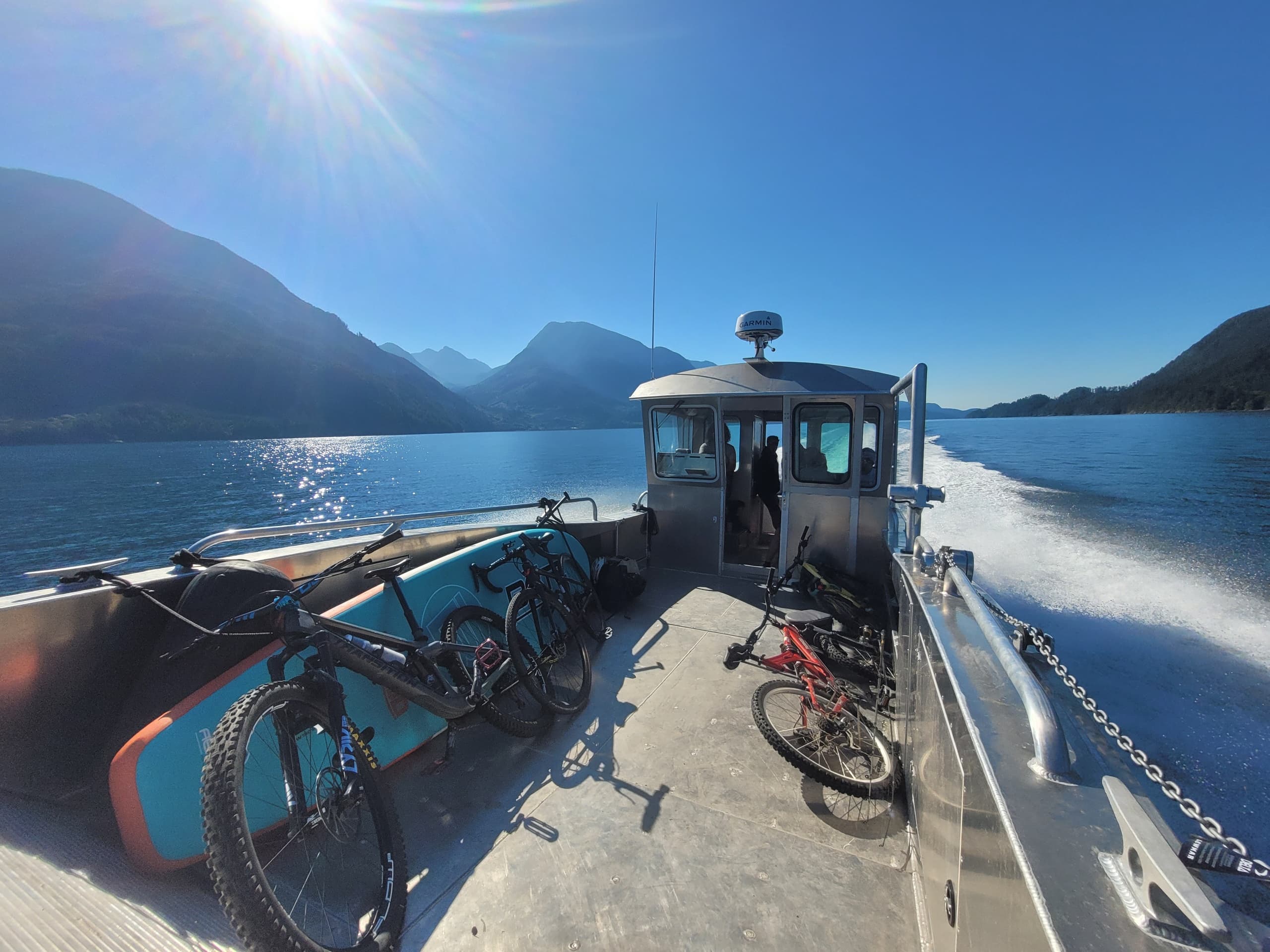Boat deck with bikes cruising sunlit fjord and mountains