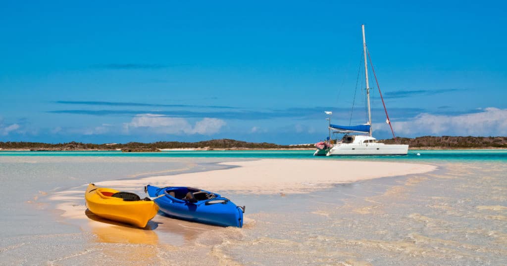 Two kayaks on white sand beach with anchored catamaran