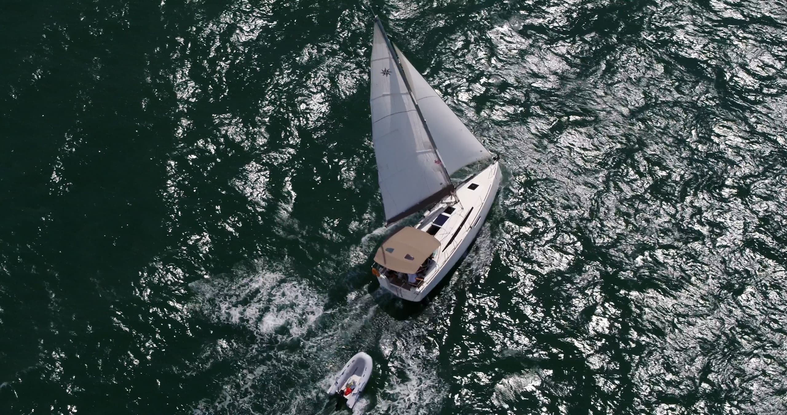 Top-down aerial sailboat over deep green ocean, dramatic angle