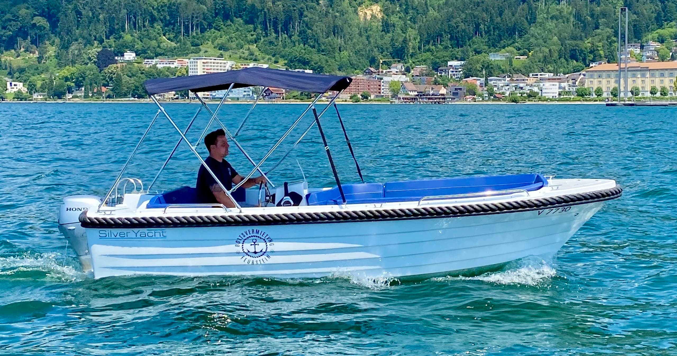 Small rental motorboat cruising near Bregenz shoreline on lake