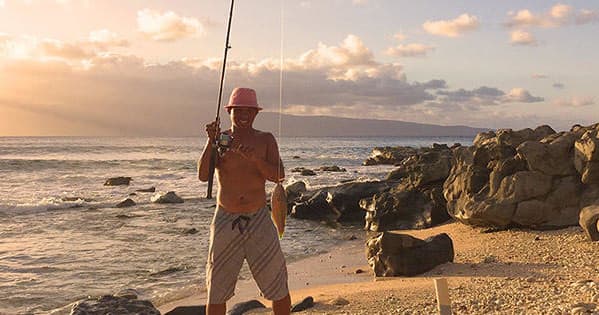 Angler on sunset beach with rocky shoreline, Hawaiian fishing